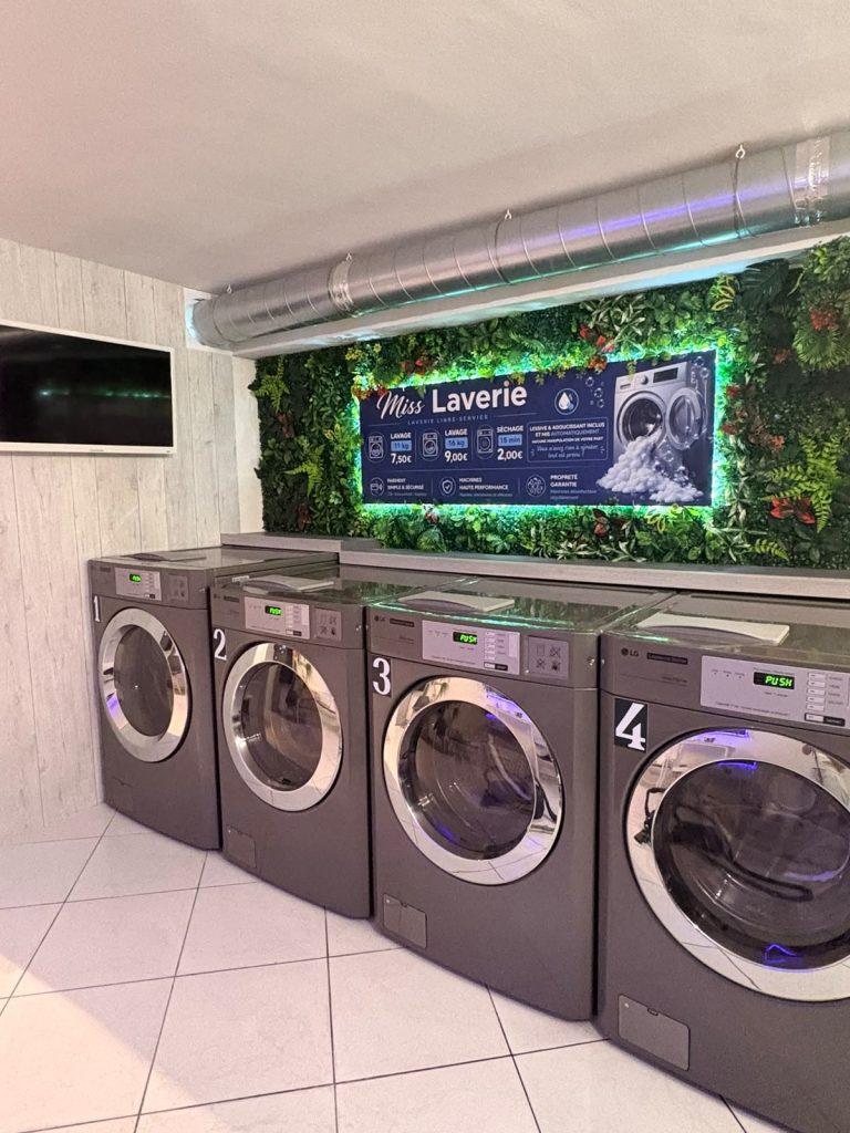 Les quatre lave-linge LG Professional de Miss Laverie sous le mur végétal et son panneau lumineux